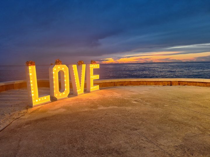 Large white marquee LOVE letters lit up with bulbs at an outdoor wedding venue in Cozumel, Mexico, overlooking the Caribbean Sea at sunset.