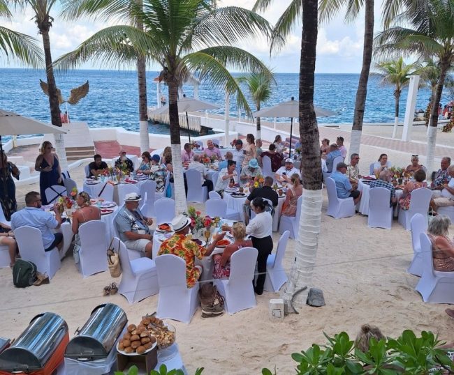 Event Planner Wedding guests enjoying an outdoor reception on a white sand beach in Cozumel, with round tables, white chair covers, and ocean views.