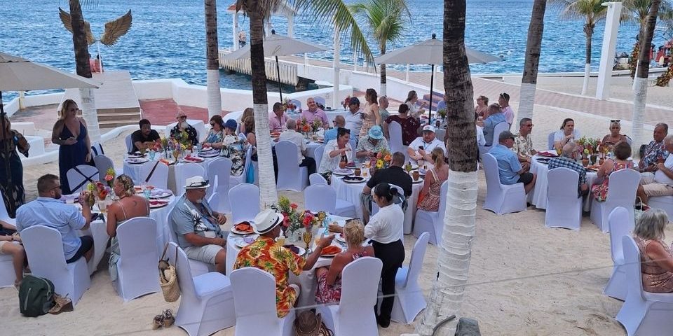 Wedding guests enjoying an outdoor reception on a white sand beach in Cozumel, with round tables, white chair covers, and ocean views.